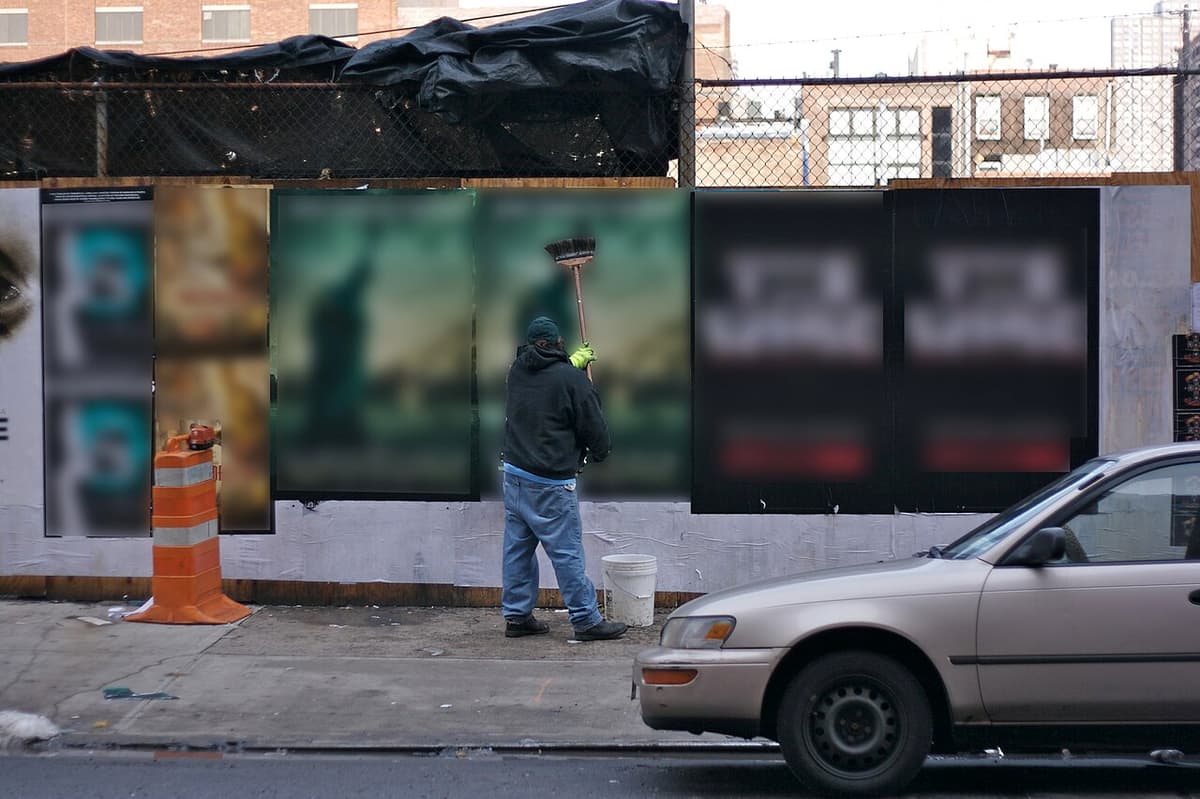 A man pasting posters onto a street hoarding